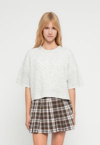 Ανοιχτό γκρι, κοντομάνικο cropped πουλόβερ με υφή, συνδυασμένο με καφέ και λευκή καρό πλισέ φούστα.