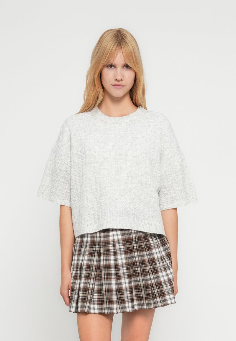 Ανοιχτό γκρι, κοντομάνικο cropped πουλόβερ με υφή, συνδυασμένο με καφέ και λευκή καρό πλισέ φούστα.