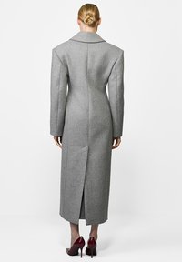 Szary wełniany płaszcz o długim fasonie, szerokich klapach i centralnym rozcięciu z tyłu. Wykończony prostymi rękawami i bez widocznych zapięć.