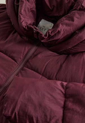 Bordová péřová bunda s vysokým límcem, vyrobená z hladkého, lesklého materiálu, s prošívanou texturou a centrálním zipem. Na etiketě je nápis "THE SET."