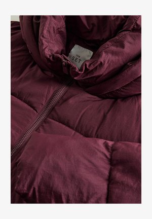 Bordeaux pufferjakke med høj krave, der har et glat, skinnende stof, quiltet tekstur og en midterlynlås. Mærket siger "THE SET."