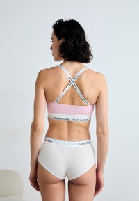 Calvin Klein sportska majica u svijetlo ružičastoj boji s kontrastnom elastičnom trakom i skliskim naramenicama, uparena s bijelim visokim gaćicama.