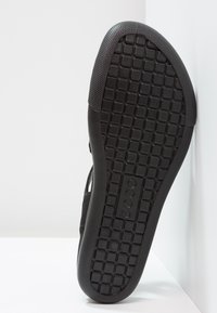 Mustat sandaalit, joissa on teksturoitu kumipohja, jossa on ruudukkomuotoilu, joustava rakenne ja EVA-välikerros mukavuutta varten. Ei näkyviä metalliosia.