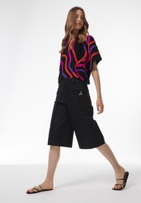 Pantalones cortos negros con grandes bolsillos y un acento decorativo de hardware, combinados con una blusa de manga corta de patrón abstracto multicolor.