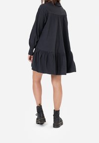 Black, textured, long-sleeve dress with a tiered hem. Paired with black, glittery ankle boots. Dress features a collar and button cuffs.