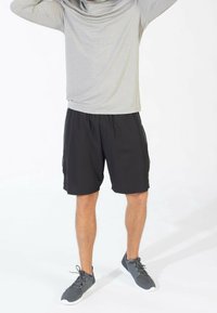 Grijze langemouwen top met een losse pasvorm, gecombineerd met zwarte sportshorts. Grijze sneakers met veters en witte zolen.