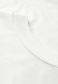 Camiseta de algodón blanca con un escote redondeado, textura suave y acabado limpio. Detalle de costura sutil a lo largo del cuello.