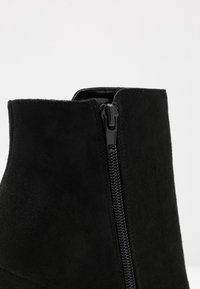 Stivaletto in suede nero con cerniera chiusa sul lato su uno sfondo chiaro e semplice.