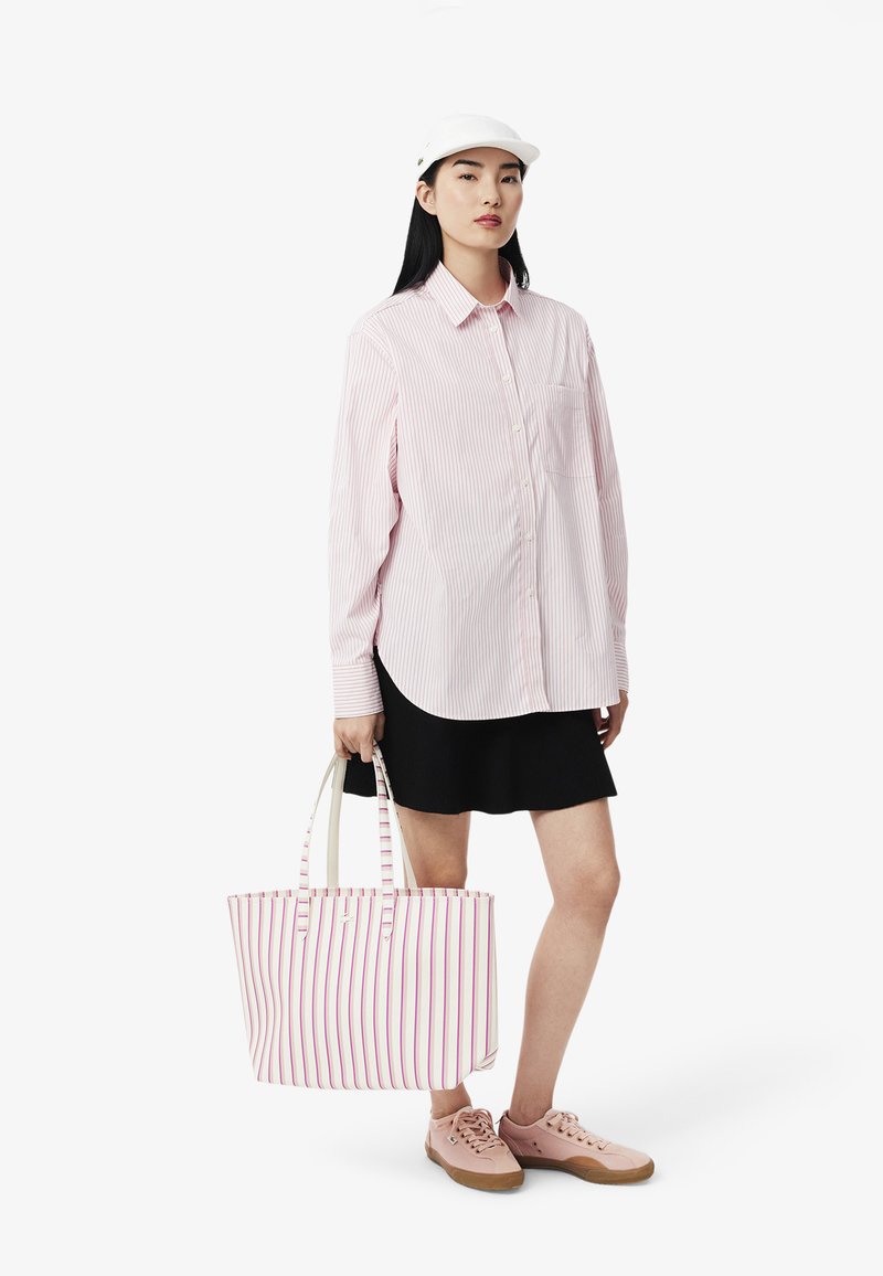 Camisa de botones a rayas rosa y blanca, falda negra, zapatillas rosas y un bolso de mano a rayas con asas claras. Look limpio y casual.