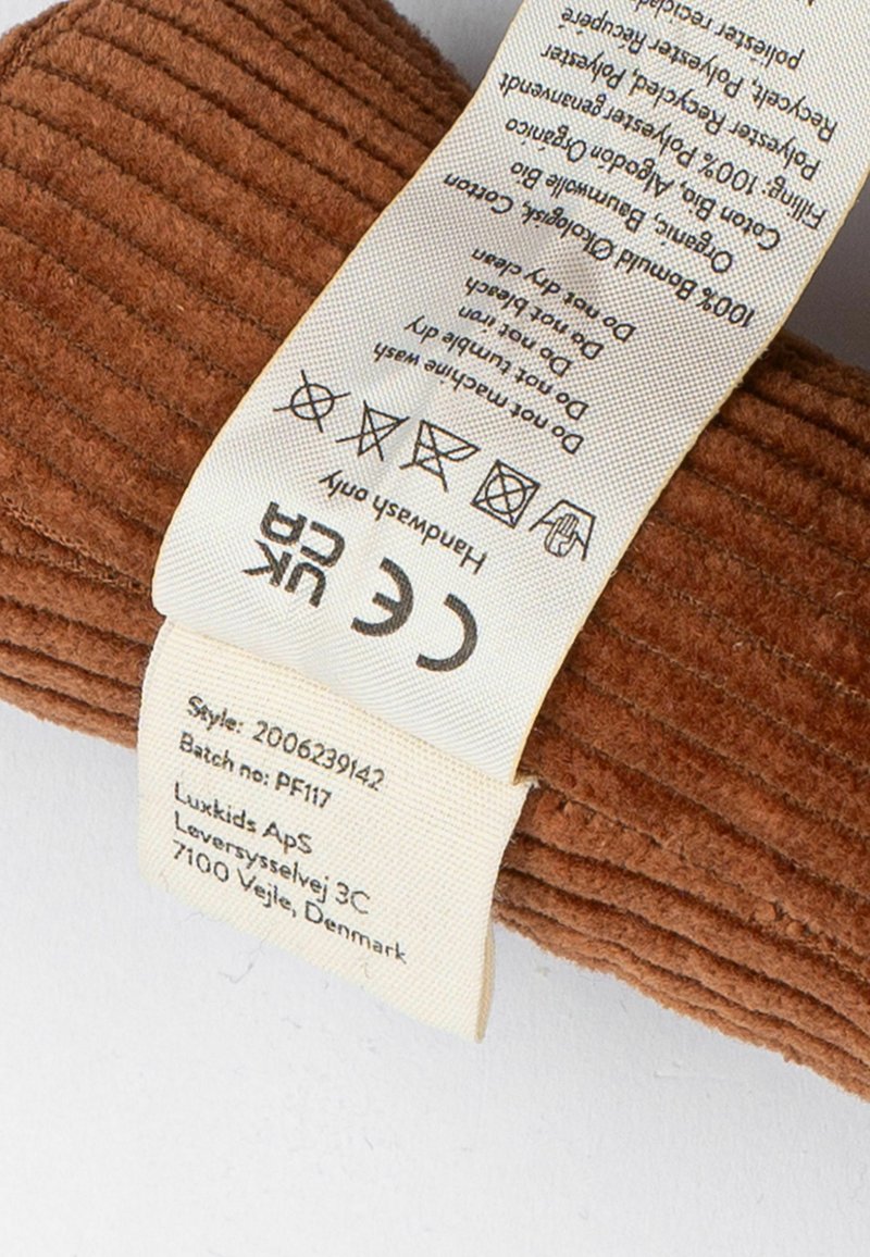 Braunes Cordstoff mit vertikalen Rippungen, mit einem angenähten Pflegeetikett. Das Etikett enthält Informationen zum Material und Pflegehinweise.
