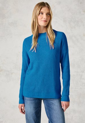 Blåtexturerad tröja med rund halsringning, långa ärmar och ribbad nederkant, ihop med ljusblå denimjeans.
