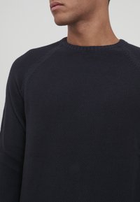 Marinblå stickad tröja med strukturerad finish, rund halsringning och raglanärmar, som framhäver en åtsittande silhuett och rena linjer.