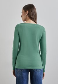 Langärmliges, grünes Oberteil aus weichem Stoff, mit einem Rundhalsausschnitt und slim fit, kombiniert mit blauen Jeans im lässigen Stil.