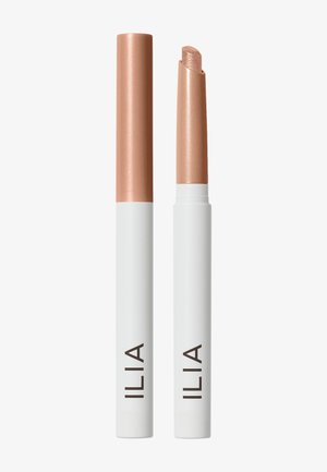 Deux tubes blancs portant la mention ILIA, l’un fermé et l’autre ouvert révélant un stick de maquillage couleur champagne scintillant sur un fond uni.