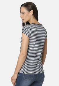 Camiseta de manga corta a rayas en azul marino y blanco con cuello redondo y diseño ajustado, combinada con jeans azules, vista desde la espalda.