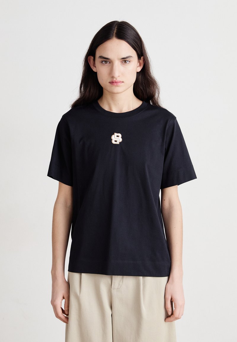 T-shirt en coton noir avec une coupe décontractée, un col rond et des manches courtes, présentant un logo accent léger sur la poitrine.