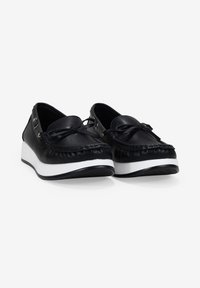 Zapatos de cuero negro con punta redonda, detalle decorativo de lazo y suela de plataforma blanca. Parte superior texturizada con borde desflecado y acentos dorados.