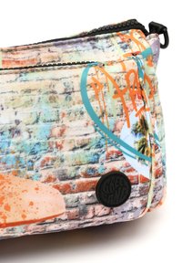 Flerfärgad vadderad påse med en texturerad yta, prydd med ett murväggstryck, orange graffiti-accenter och ett runt svart logomärke.