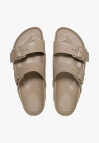 Tan sandalen met twee verstelbare gespsluitingen, gemaakt van glad synthetisch materiaal. Gecurveerde voetbed en vlakke zoolontwerp.