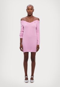Robe tricotée rose avec un décolleté en V et des bretelles tombantes. Présente des poignets et un ourlet côtelés, ainsi qu'une silhouette ajustée. Associe à des chaussures métalliques.