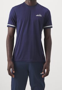 Námorně modré sportovní tričko s krátkým rukávem a bílými pruhovanými akcenty na rukávech. Vyrobeno z hladké, prodyšné tkaniny. Obsahuje malé logo na hrudi.