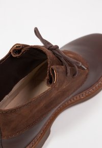 Zapato de cuero marrón con una parte superior de ante texturizado, cierre con cordones y una suela de goma sólida con detalle de costura en el borde.
