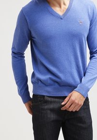 Helles blaues V-Ausschnitt-Pullover aus Strickmaterial, mit einer enganliegenden Passform und gerippten Bündchen und Saum. Kleines Logodetail auf der Brust.