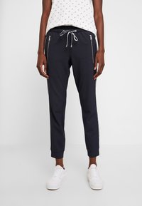 Marinblå joggerbyxor i texturerad tyg, med sidofickor med dragkedja, dragsko i midjan och elastiska muddar. Vita sneakers fulländar looken.