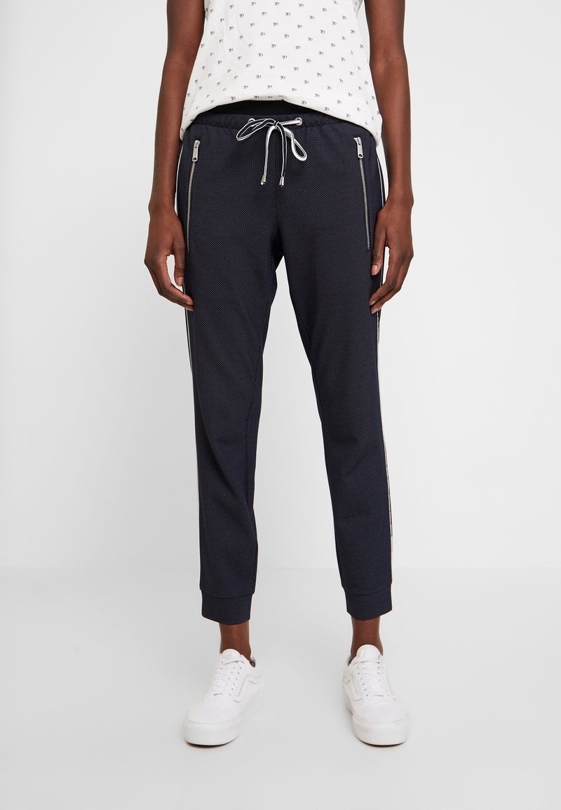 Marinblå joggerbyxor i texturerad tyg, med sidofickor med dragkedja, dragsko i midjan och elastiska muddar. Vita sneakers fulländar looken.