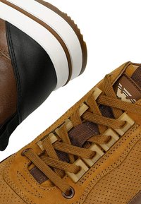 Sneaker in pelle marrone con una parte superiore texturizzata, lacci marroni e suola in gomma bianca. Inclusa un'accento nera sul tallone.