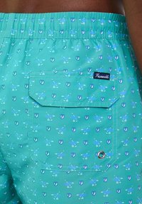 Pantaloni da bagno turchesi con un vivace motivo di piccole frecce blu e una tasca a patta, caratterizzati da un'etichetta del marchio e un dettaglio con occhiello in metallo.