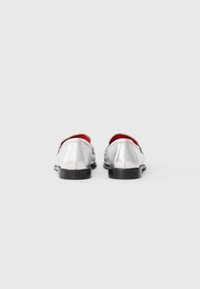 Silver loafers with a glossy finish, black soles, and red interior. Rounded toe design and open back for easy wear.
