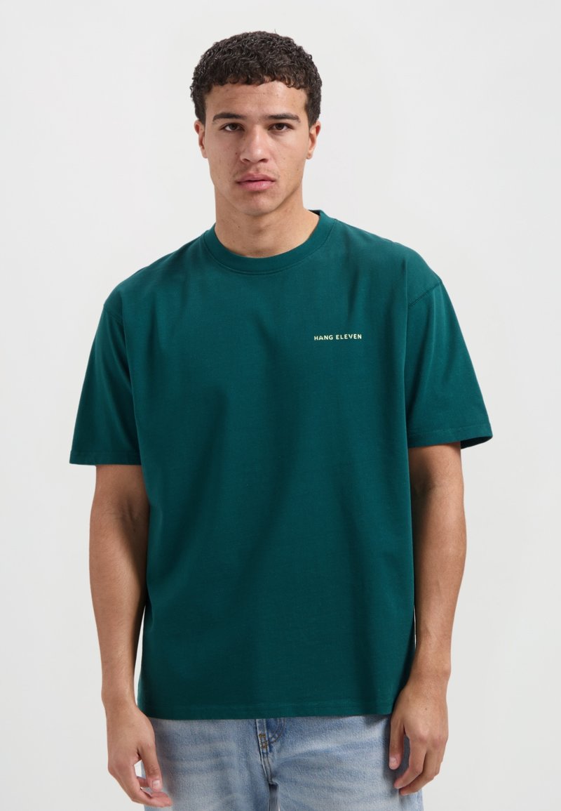 Teal katoenen t-shirt met een ronde hals en korte mouwen. Bevat een klein "HANG ELEVEN" logo in het geel op de linkerborst. Eenvoudig ontwerp.
