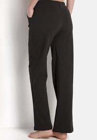 Schwarze, locker sitzende Hosen aus weich gewebtem Stoff, mit Seitentaschen und einem Bund ohne sichtbare Befestigungen. Entworfen für maximalen Komfort.