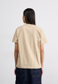 T-shirt beige à col rond avec des manches courtes, fabriqué en tissu de coton doux. Présente une coupe décontractée et une texture lisse, sans embellissements.