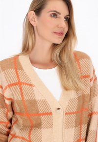 Cardigan beige con motivo a scacchi arancioni, design a scollo a V e chiusura con un solo bottone. Realizzato in tessuto morbido e texturizzato.