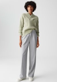 Light green knitted sweater with a split V-neck, paired with high-waisted, light gray pleated trousers and white sneakers.