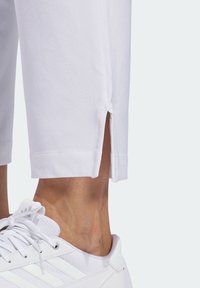 Vita avklippta byxor i mjukt tyg med sidoklipp vid fållen, i kombination med vita sneakers med tre ränder på sidan.