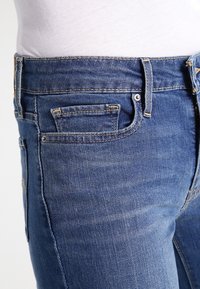 Modré džíny z denimu s přiléhavým střihem, se malou přední kapsou, viditelným prošíváním a hladkým povrchem.