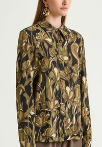 Langärmlige Bluse aus dunklem Stoff mit großen grünen und cremefarbenen Blumenmustern, vorne mit Knöpfen und klassischem Kragen.