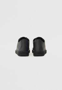 Fekete bőr sportcipő, texturált felülettel, alacsony profilú, gumitalppal. Kialakítása slip-on stílusú, látható fűzők vagy hardver nélkül.
