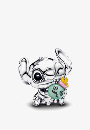 Piccola figurina d'argento di un personaggio con grandi orecchie che tiene una bambola verde con dettagli cuciti e un accessorio rosa e giallo.