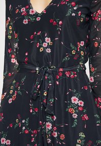 Blumenkleid mit tiefem V-Ausschnitt, langen durchsichtigen Ärmeln und einem Bindegürtel in der Taille. Hat einen dunklen Hintergrund mit mehrfarbigen Blumenmustern.