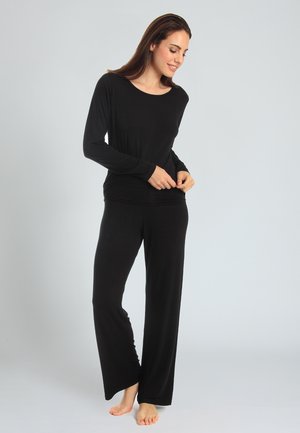 Maglietta nera a manica lunga con scollatura ampia abbinata a pantaloni neri a gamba larga, realizzati in materiale morbido ed elastico.