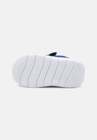 Baskets bleues avec une tige en tissu texturé, semelle extérieure en caoutchouc blanc et rainures distinctes. Équipées d'une languette pour un enfilage facile.