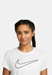 Camiseta blanca de manga corta con un gran logo negro de Nike Swoosh en el pecho. La modelo tiene el cabello trenzado y una expresión neutral.