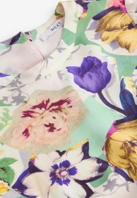 Blusa con motivo floreale in tessuto leggero. Presenta fiori viola, gialli e rosa su uno sfondo verde e crema. Collo rotondo.