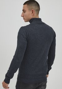 Marineblå turtleneck genser, ribbestrikkede mansjetter og nederkant, tettsittende design, strukturert strikket stoff, sett fra baksiden som fremhever skuldersøm.