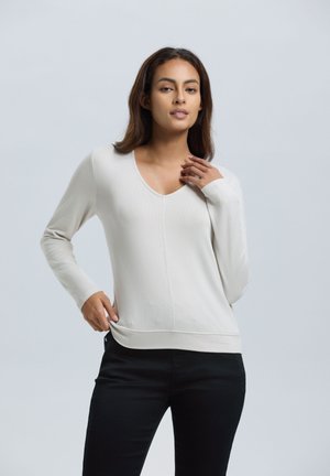 Lichtbeige, lange mouw, V-hals trui, geribbeld textuur, aansluitende pasvorm, met een gladde afwerking en een naaddetail aan de voorkant, gecombineerd met zwarte broek.