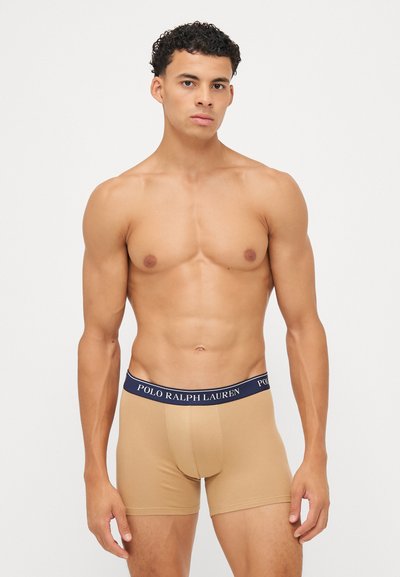 Boxer briefs bege com um cós elástico azul-marinho apresentando o logótipo "POLO RALPH LAUREN", tecido suave, design ajustado e comprimento até meio da coxa.
